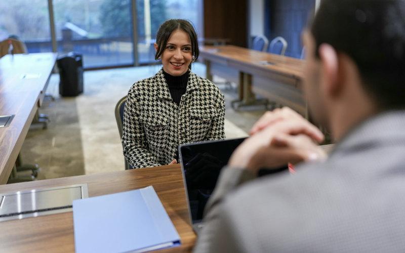 Dank optimaler Bewerbungsmappe sitzt eine junge Frau beim Vorstellungsgespräch in einem Meetingraum ihrem potenziellen neuen Chef gegenüber.