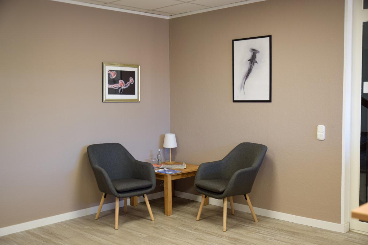 Gemütliche Sitzecke bei Nordwest Training mit zwei Sesseln, einem kleinen Ecktisch mit Lampe und zwei Bildern darüber.